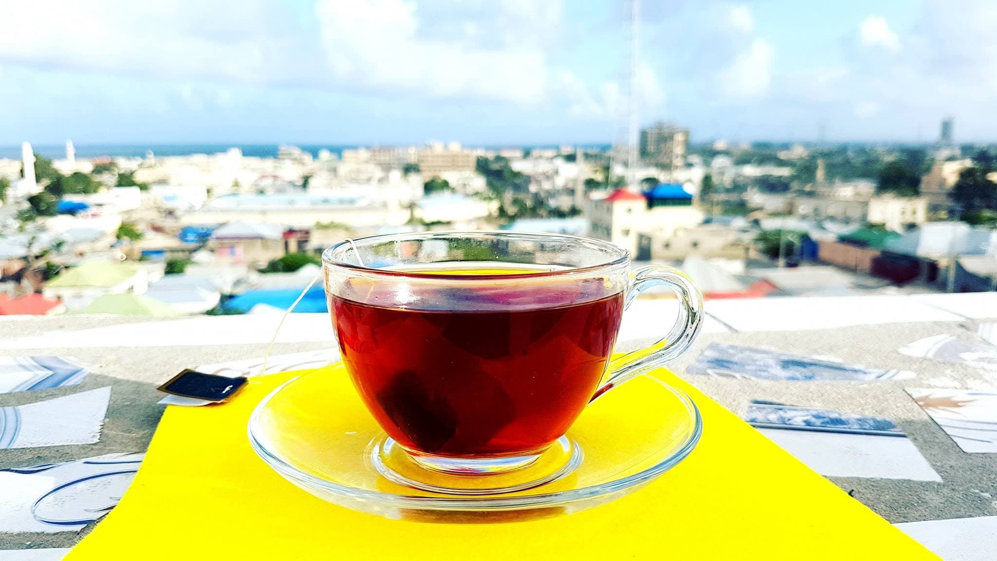 A glass of Somali shaah in the foreground, overlooking the Mogadishu skyline, rendered in ink and gold duotone.