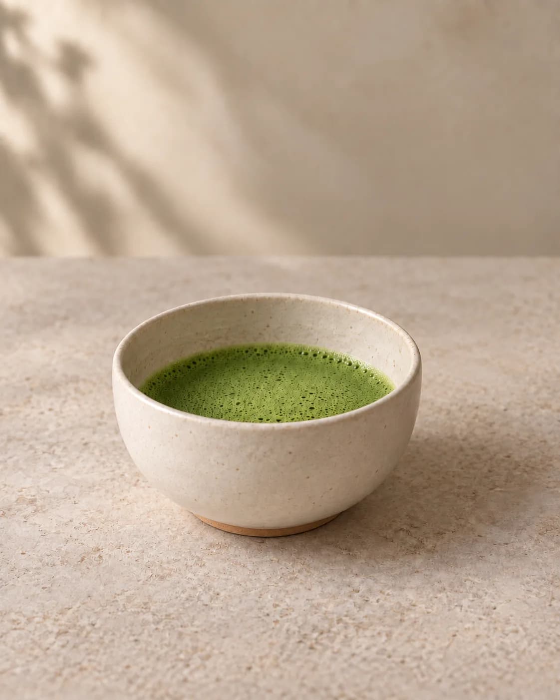 A wide ivory bowl of bright whisked matcha beside a bamboo whisk on its stand.